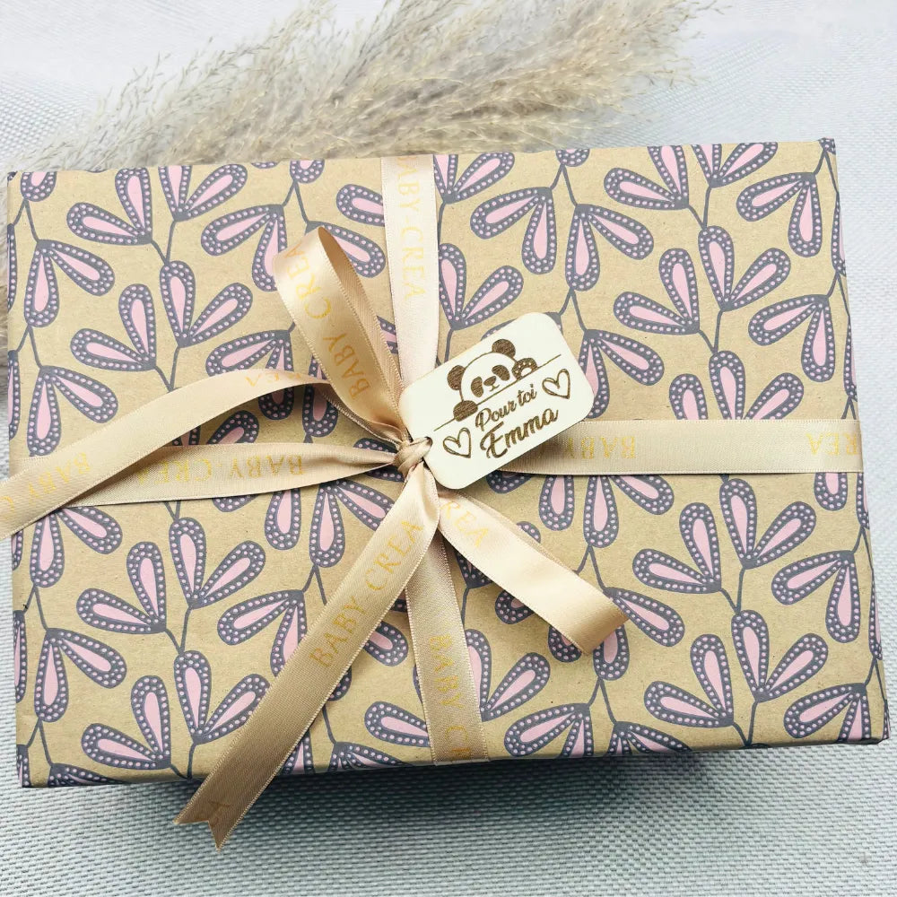 Emballage cadeau de naissance personnalisé avec ruban BABY-CREA et étiquette gravée 'Pour toi Emma', parfait pour un coffret bébé fille – papier fleuri rose et beige, idéal pour un cadeau de naissance unique et élégant.