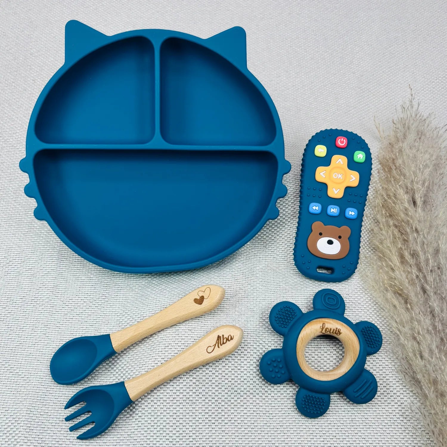 Coffret repas bébé bleu personnalisé avec prénom, assiette en silicone chat, cuillère et fourchette en bois gravé, jouet d'éveil en silicone et télécommande sensorielle. Cadeau naissance unique.