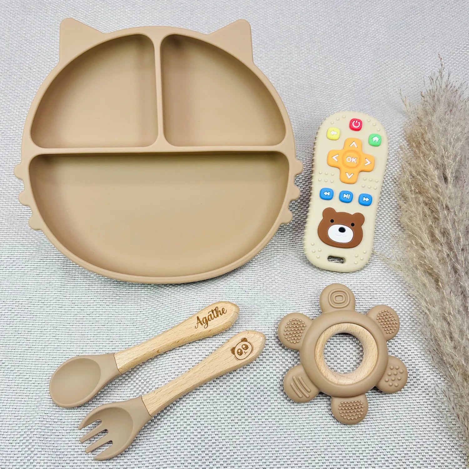 Coffret repas bébé couleur beige avec assiette ventouse, couverts bois gravés au prénom Agathe, jouet dentition et télécommande. Idéal comme coffret cadeau bébé personnalisé.
