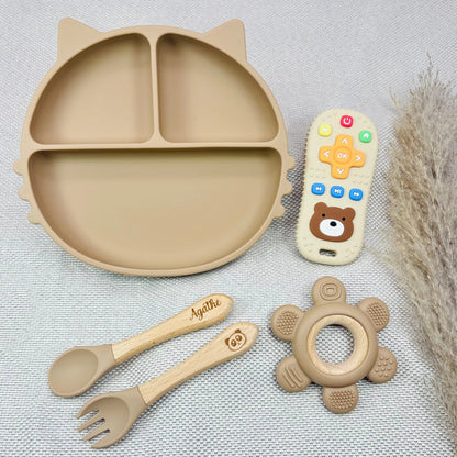 Coffret repas bébé couleur beige avec assiette ventouse, couverts bois gravés au prénom Agathe, jouet dentition et télécommande. Idéal comme coffret cadeau bébé personnalisé.