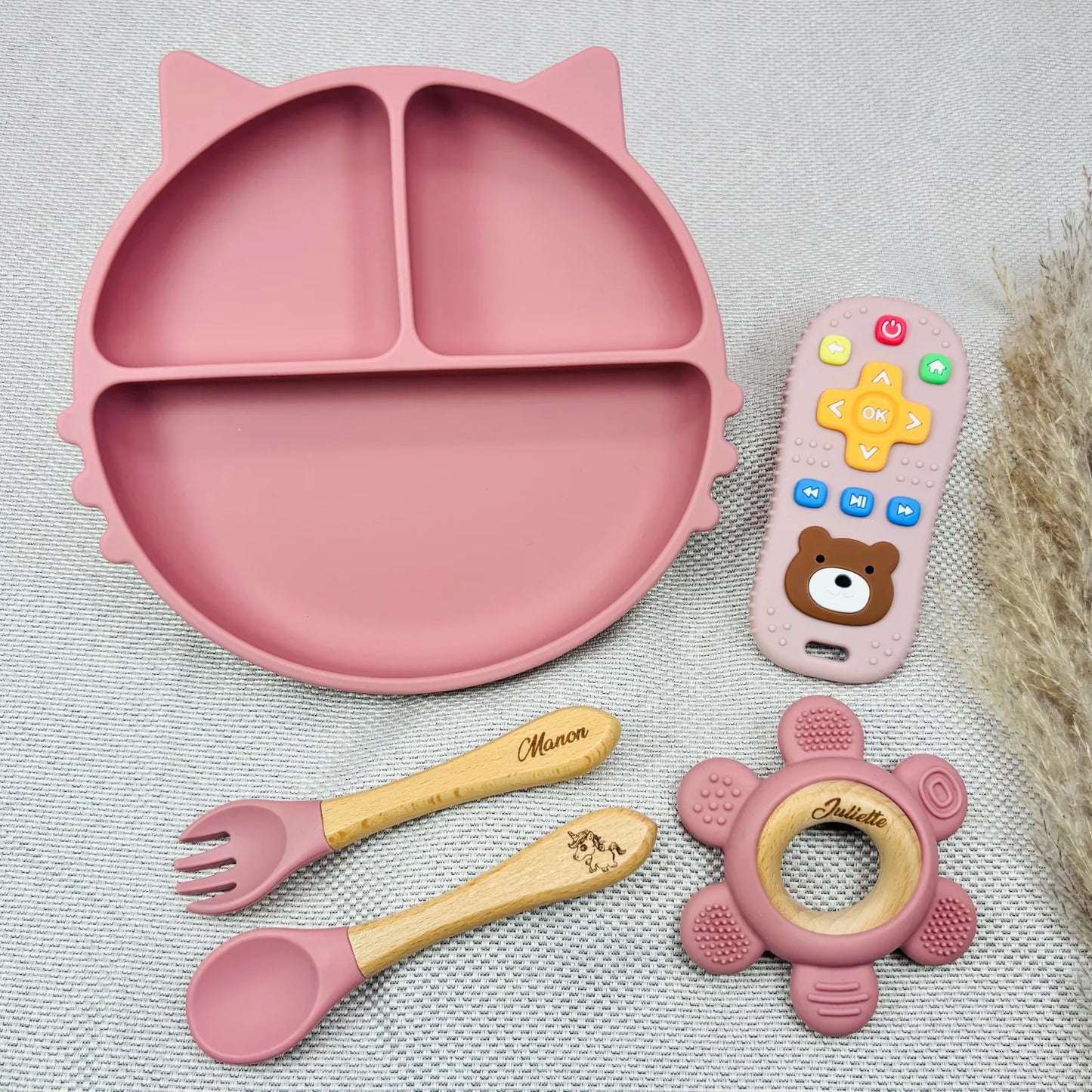 Coffret repas bébé rose personnalisé avec prénom Manon et Juliette, comprenant assiette chat antidérapante, jouet d’éveil et couverts bois. Idée cadeau bébé fille.