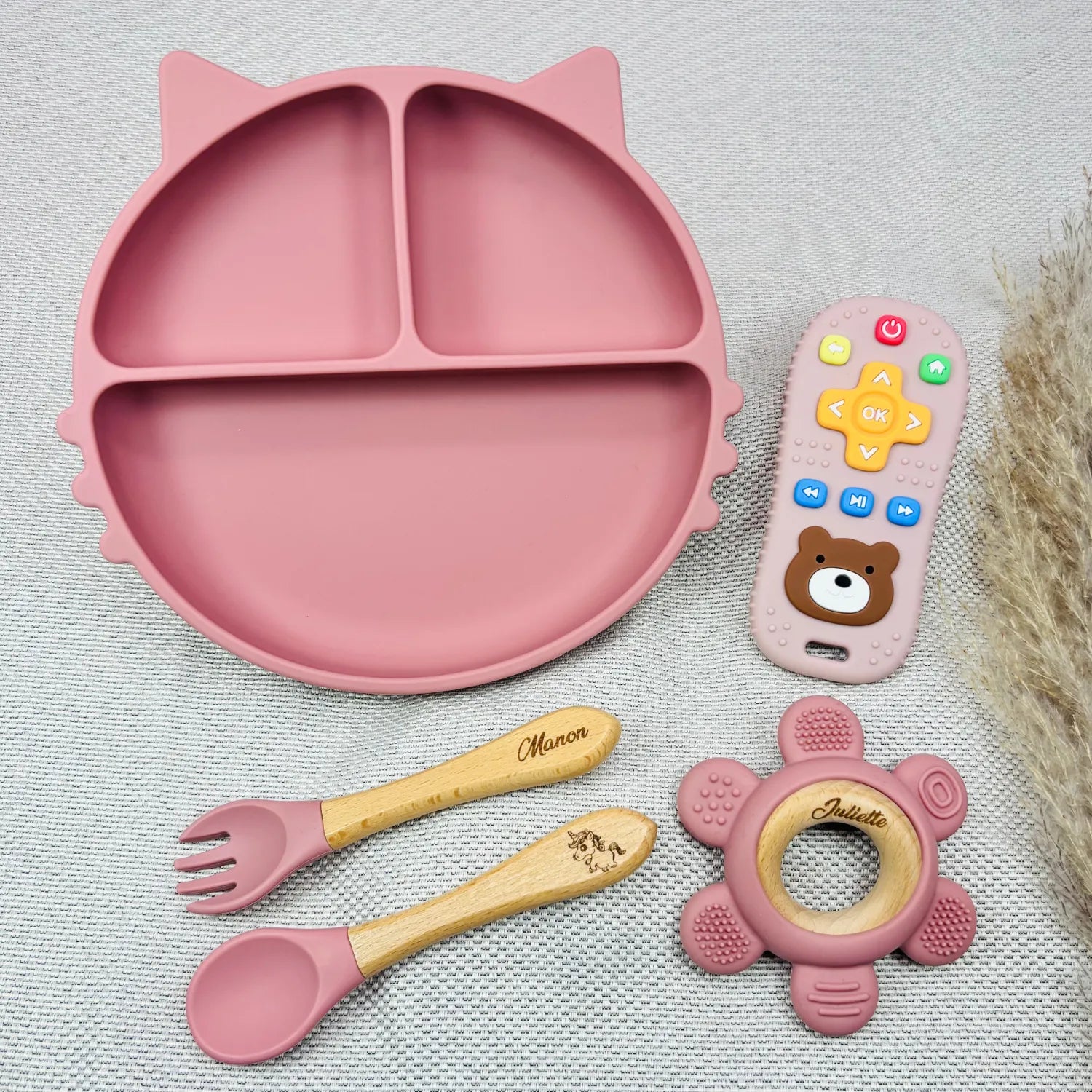 Coffret repas bébé rose personnalisé avec prénom Manon et Juliette, comprenant assiette chat antidérapante, jouet d’éveil et couverts bois. Idée cadeau bébé fille.
