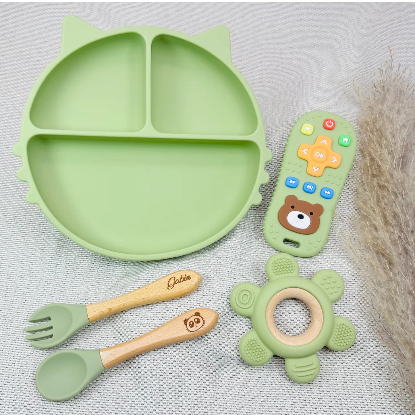 Kit repas bébé vert pastel avec assiette silicone, cuillère et fourchette prénom Gabin gravé, jouet en bois/silicone et télécommande sensorielle. Cadeau de naissance tendance.
